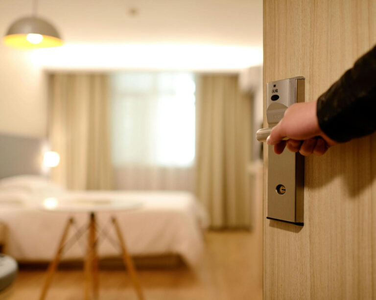 person holds open the door to a cozy hotel room.