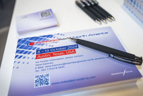 Flyer for "Embedded World North America" in Austin, Texas, on October 8-10, 2024, with event details, contact info, and a QR code, alongside a black pen.