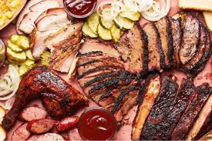 A platter of various barbecued meats with sides and dipping sauces.