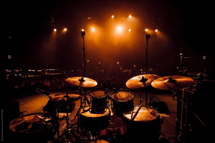 A drum set on stage under warm lights, facing an audience.